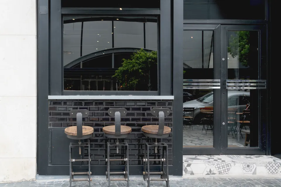 A café entrance with large glass windows and bar stools along the front