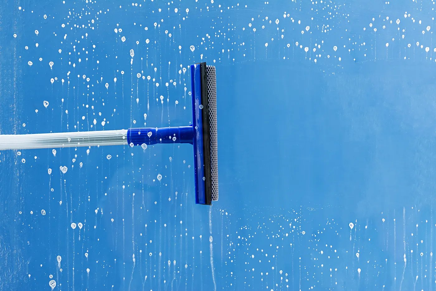A blue squeegee clearing soap and water from a pane of glass